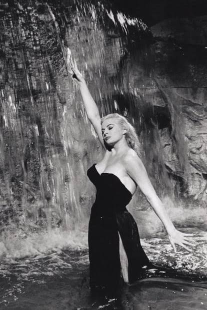 Mujer con vestido negro posando bajo una cascada, mientras el agua cae a su alrededor en un ambiente dramático en blanco y negro.